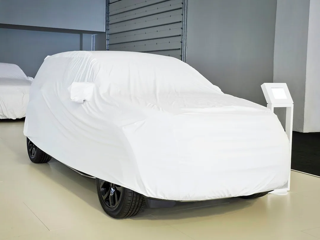 Two cars under fitted white covers in a bright showroom